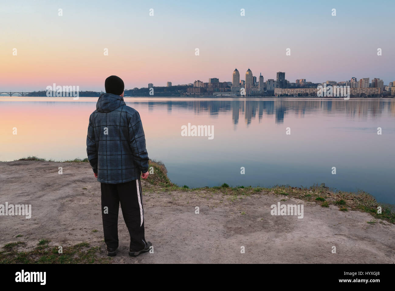 Le gars répond à l'aube debout sur la rive du fleuve et à la route dans la ville Banque D'Images