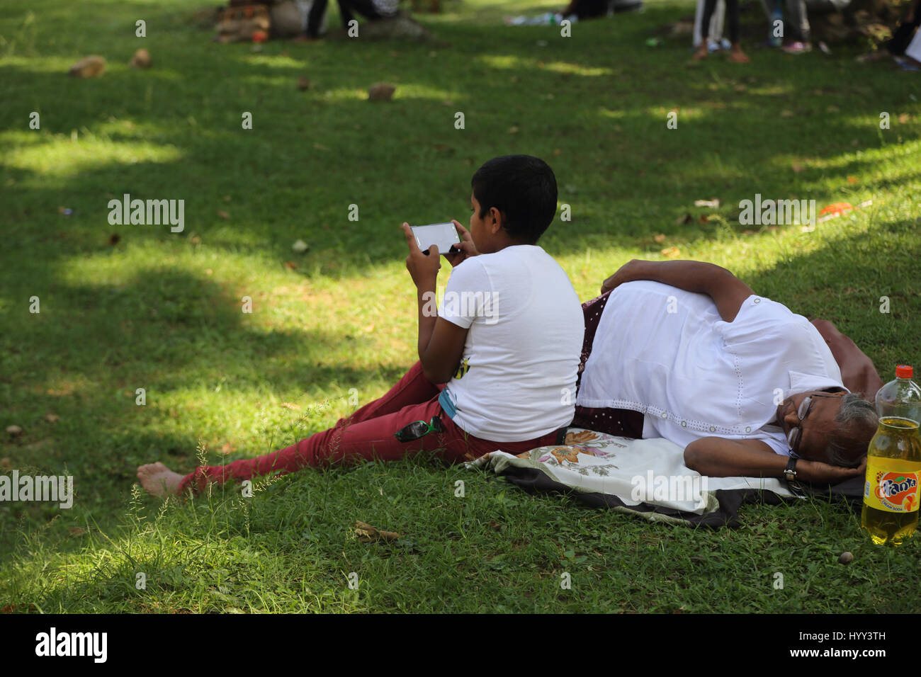 Aluviharaya Rock Cave Temple Sri Lanka- Kandy-Dambulla District l'autoroute Mother and Boy Sitting on Grass Looking at Mobile Phone sur écran Banque D'Images