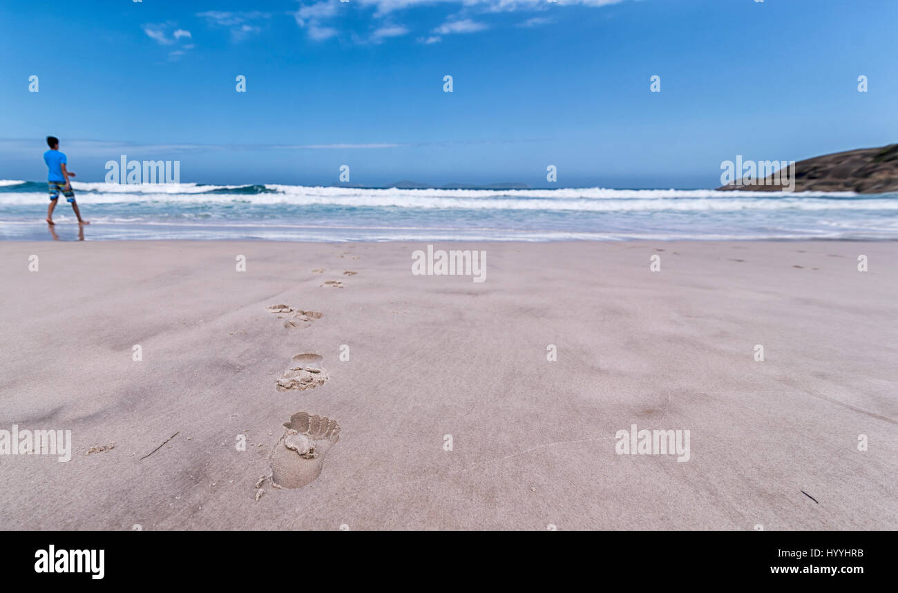 Un portrait d'une plage de sable avec des empreintes de pieds menant vers les vagues avec un ciel bleu menant vers l'horizon. Ici, dans l'horizon. Banque D'Images