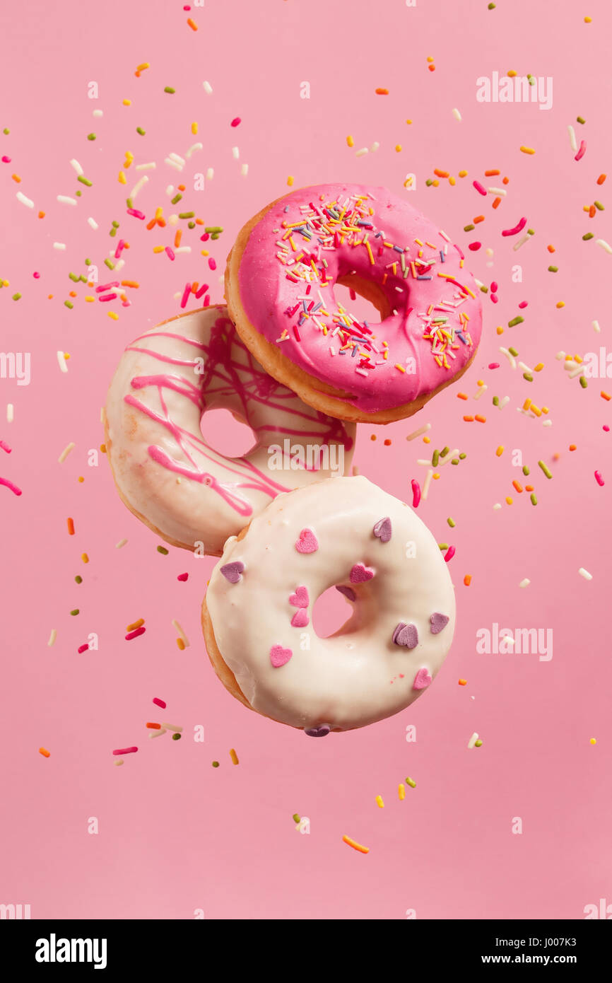 La décoration divers beignets dans motion relevant sur fond rose. Beignets sucrés et colorés en mouvement qui tombent ou qui volent. Banque D'Images