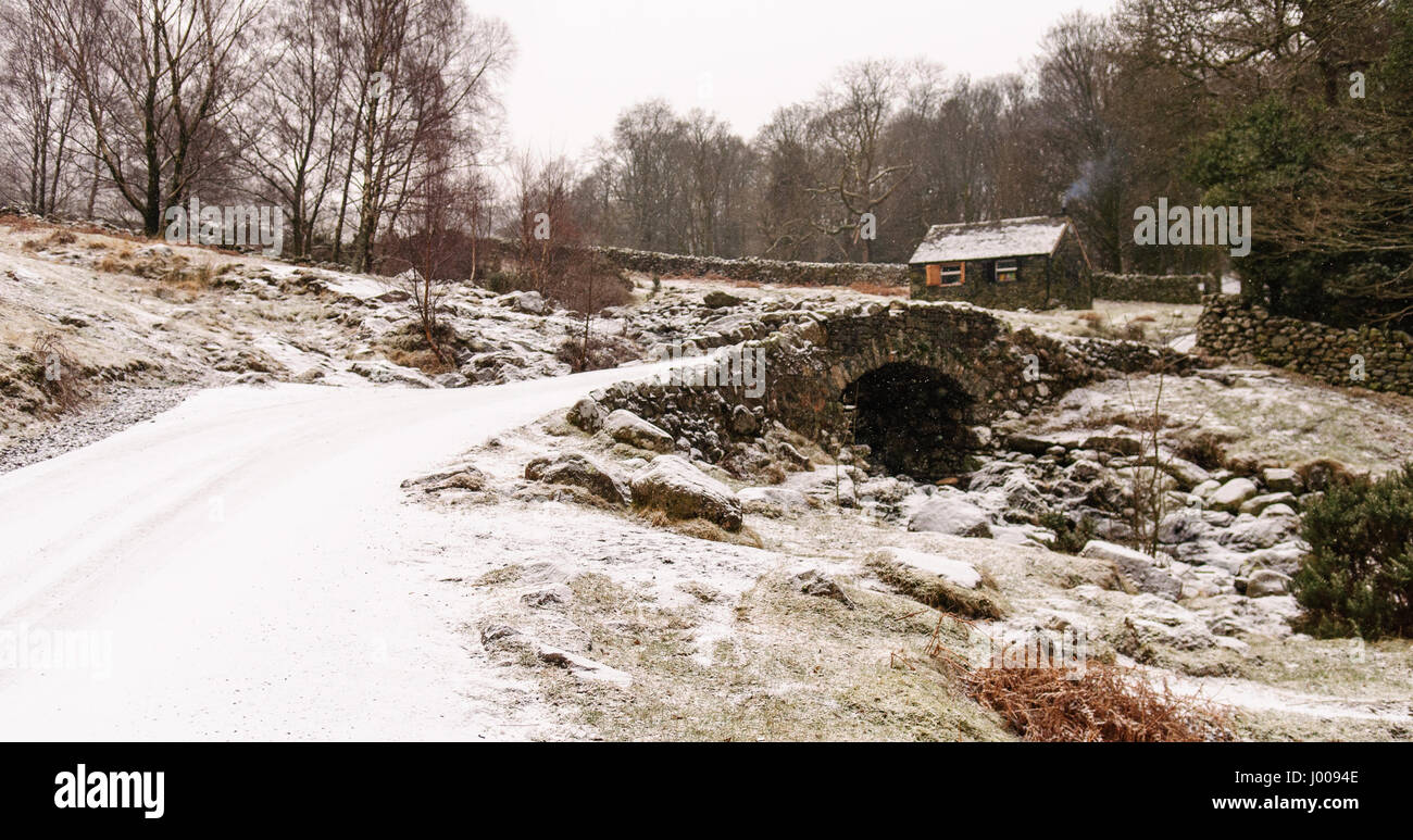 Neige de l'hiver se trouve sur le pittoresque pont voûte en pierre et grange traditionnelle à Ashness dans les bois au-dessus de la Derwent Water Lake District Banque D'Images