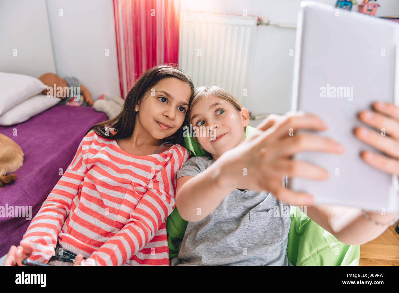 Deux filles assis dans la chambre d'enfant et en tenant avec selfies digital tablet Banque D'Images