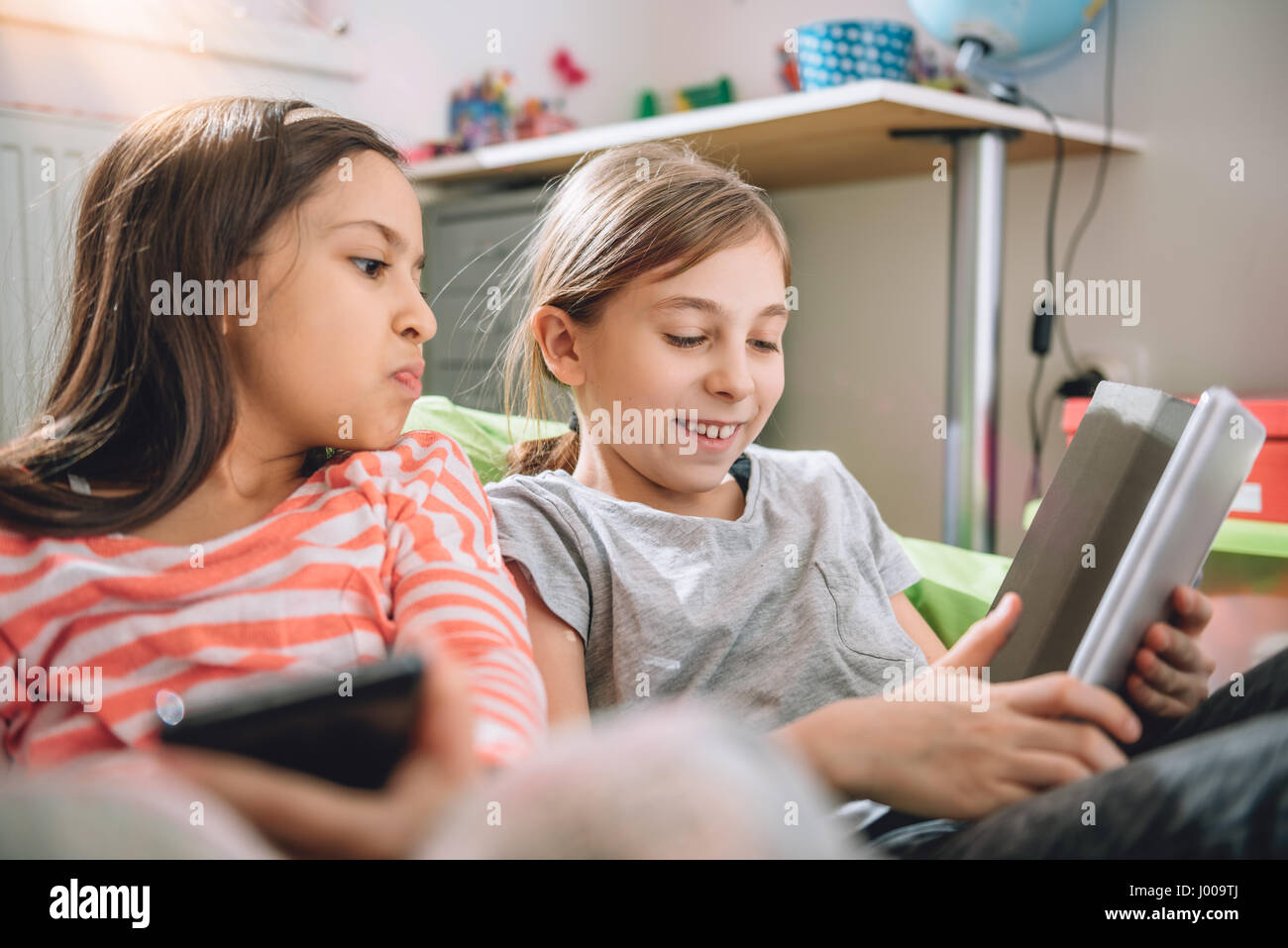 Deux filles assis dans la chambre d'enfant et using digital tablet Banque D'Images