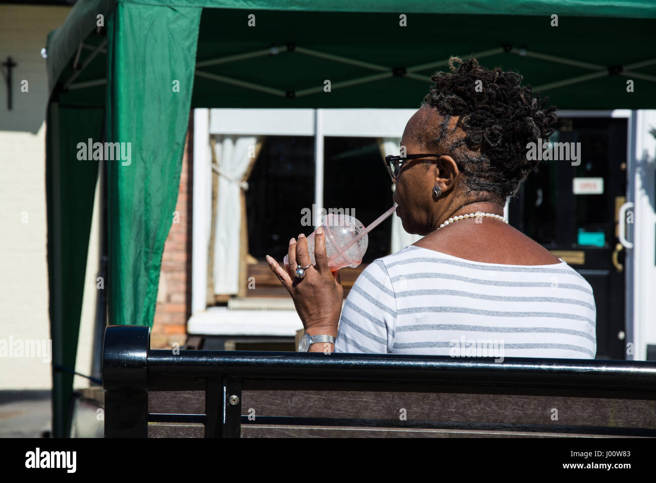 Femme à boire un smoothie profitant de la journée la plus chaude de l'année dans la ville médiévale de Much Wenlock. Banque D'Images