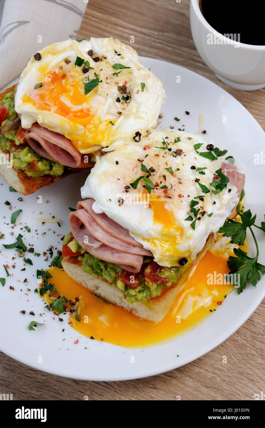 Œufs pochés à l'avocat, des tomates, des tranches de jambon sur une baguette pour le petit déjeuner Banque D'Images