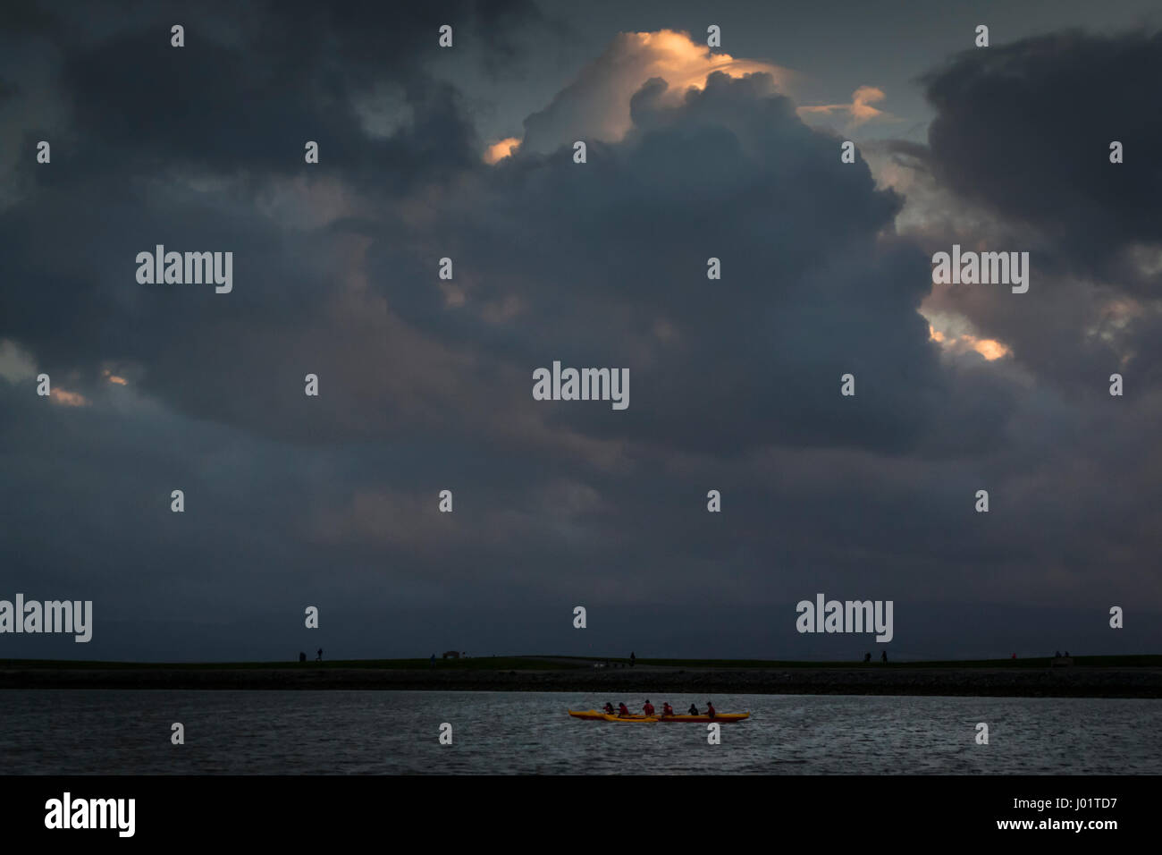 Sous un ciel encombré de nuages, une pirogue rouge et jaune fait un passage à travers le petit bateau lagoon à San Leandro Marina Park sur la baie de San Francisco Banque D'Images