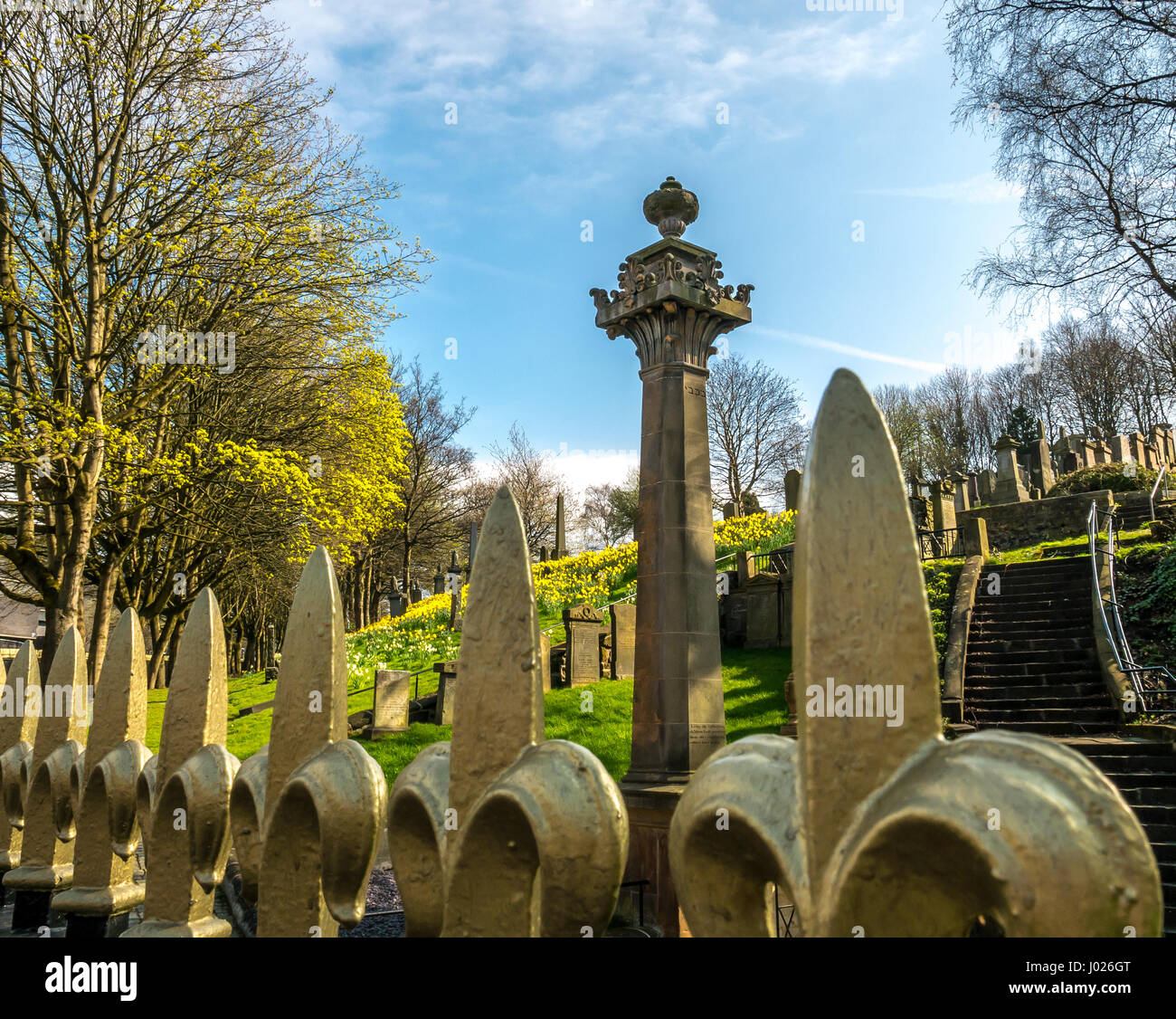 Haut d'une balustrade en fer ornemental avec fleur de lys d'or en ligne de premier plan avec des pierres tombales et grand monument à Glasgow necropolis Banque D'Images