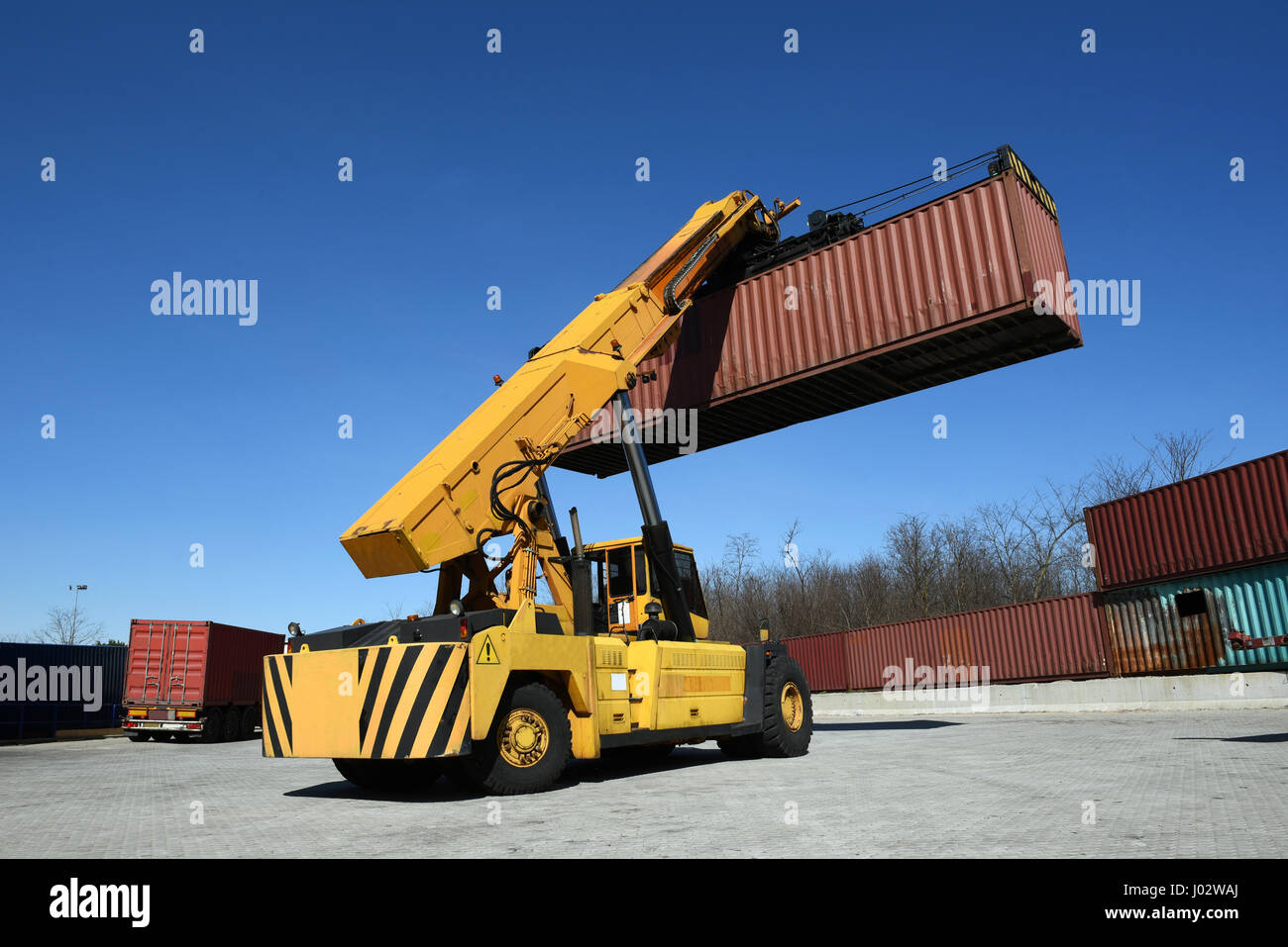 Vue arrière de la manutention des conteneurs jaune véhicule transportant des conteneurs big red en l'air, low angle view contre ciel bleu clair Banque D'Images