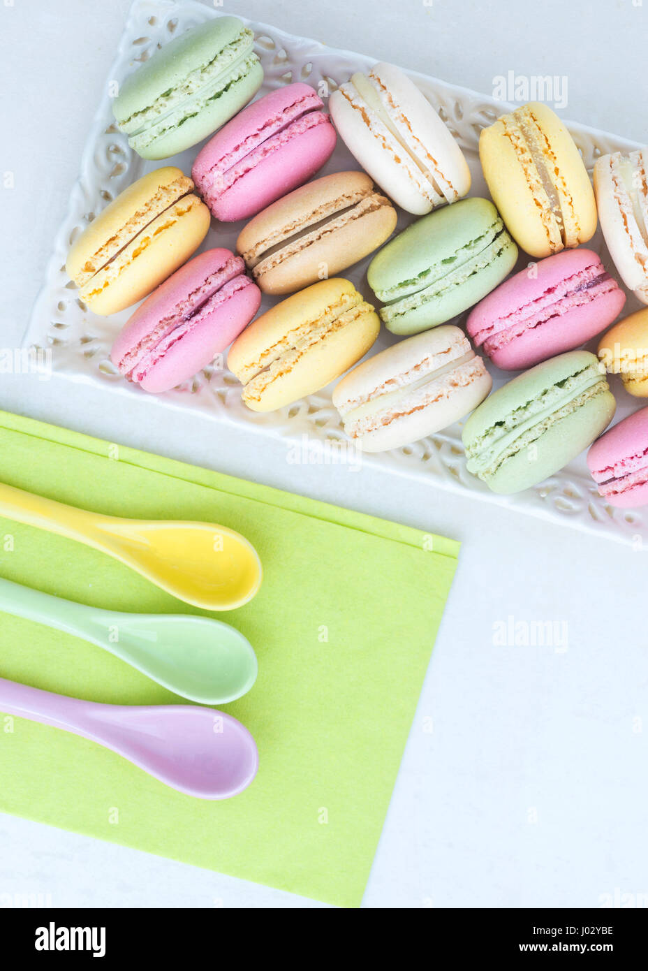 Assortiment de macarons de couleur bonbon organiser dans un joli plateau avec une serviette de couleur vert lime et cuillères. l'image est verticale et a copy space Banque D'Images