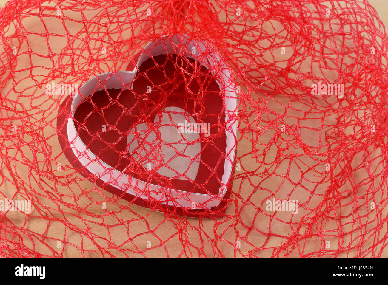 Tomber en amour ou rouge et blanc coeur capturés en filet rouge pour la Saint-Valentin Banque D'Images