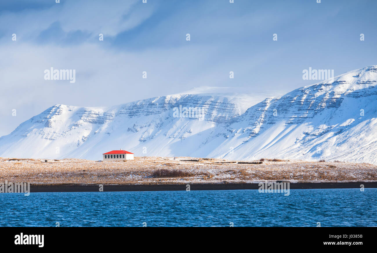 Paysage islandais côtières avec les montagnes enneigées et living house sous ciel bleu dramatique. Région de Reykjavik, Islande Banque D'Images