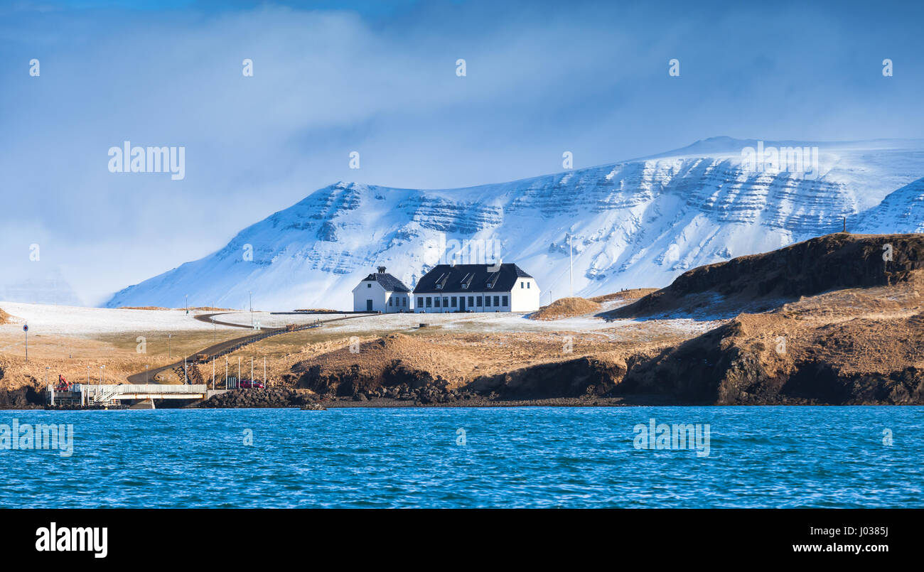 Paysage islandais côtières avec les montagnes enneigées et white living house sous ciel bleu dramatique. Région de Reykjavik, Islande Banque D'Images