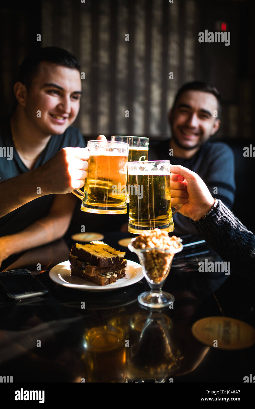 Les gens, les hommes, les loisirs, l'amitié et de fête concept - heureux amis boire une bière et clinking glasses au bar ou au pub Banque D'Images