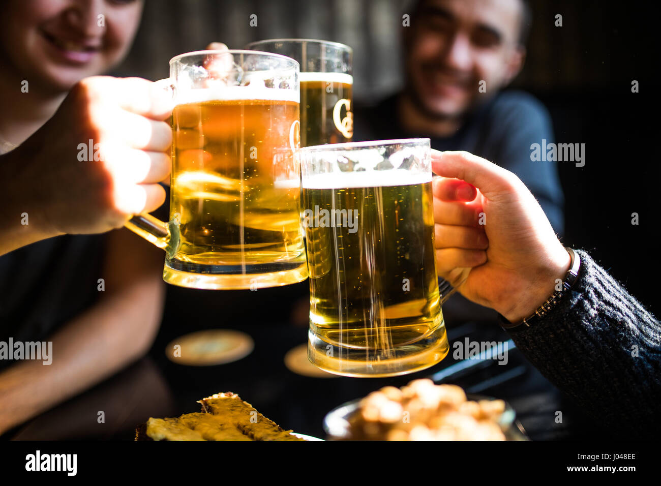 Trois jeunes hommes sont souriants et qui retentit verres de bière ensemble tout en restant assis dans un pub Banque D'Images