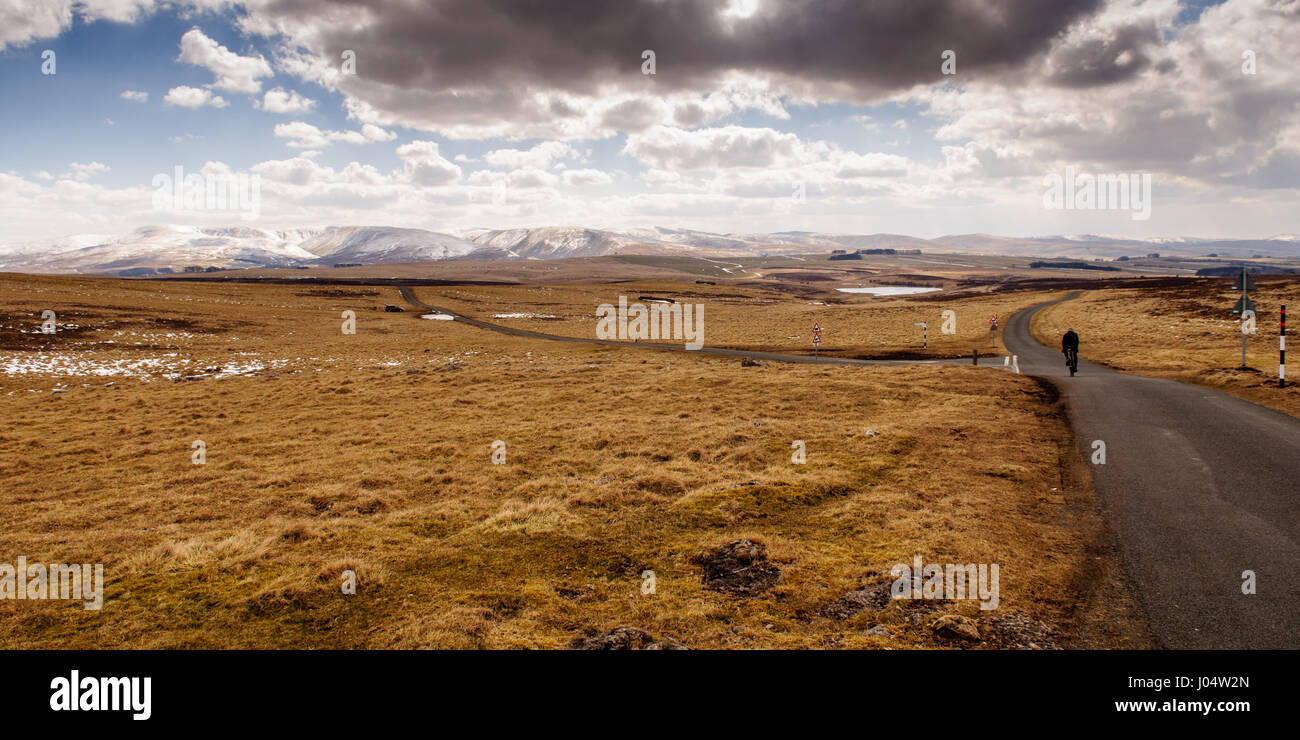 Un cycliste solitaire traverse la télécommande mais Sunbiggin ensoleillée Moors, vers les sommets enneigés des montagnes dans le Cap Sud Fells Eden district de Cumbria. Banque D'Images