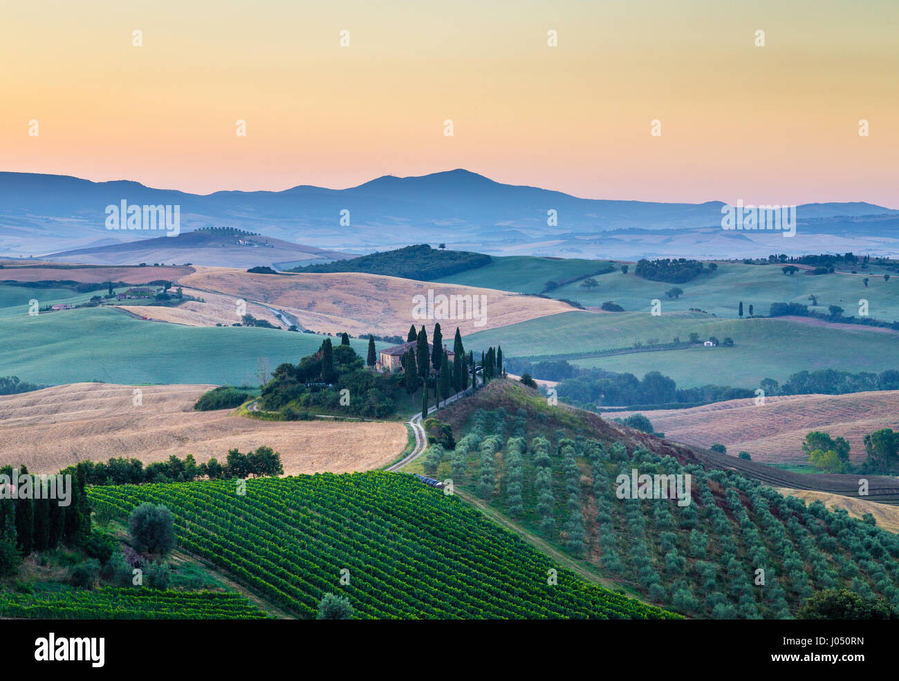 La vue classique du paysage pittoresque de la Toscane avec célèbre ferme au milieu de collines et de vallées idylliques dans la belle lumière du matin au lever du soleil d'or Banque D'Images