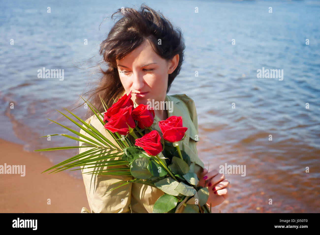 Femme de rêve avec des roses rouges contre la mer à jour ensoleillé. Brunette dans une demi-saison, à l'extérieur. Dating, romance et thème souvenirs Banque D'Images