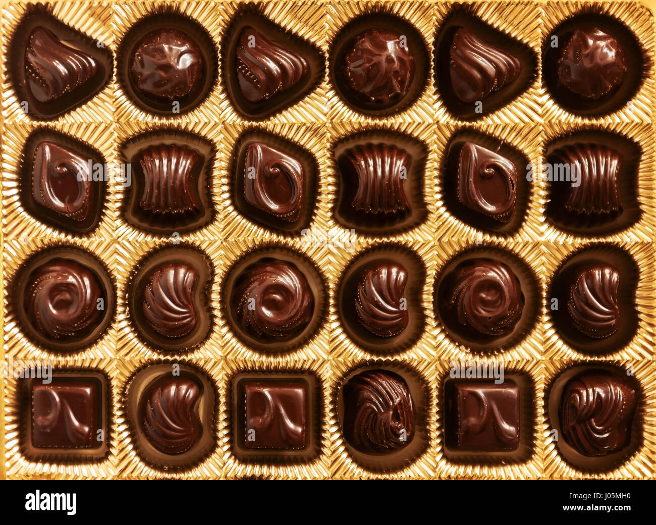 Bonbons de chocolat de formes différentes dans une boîte en or, vu de dessus, lisse les lignes symétriques pour l'arrière plan. Banque D'Images