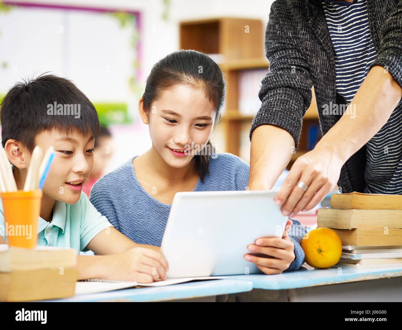 Deux enfants de l'école primaire à l'aide de tablette numérique avec l'aide de tuteur enseignant en classe. Banque D'Images