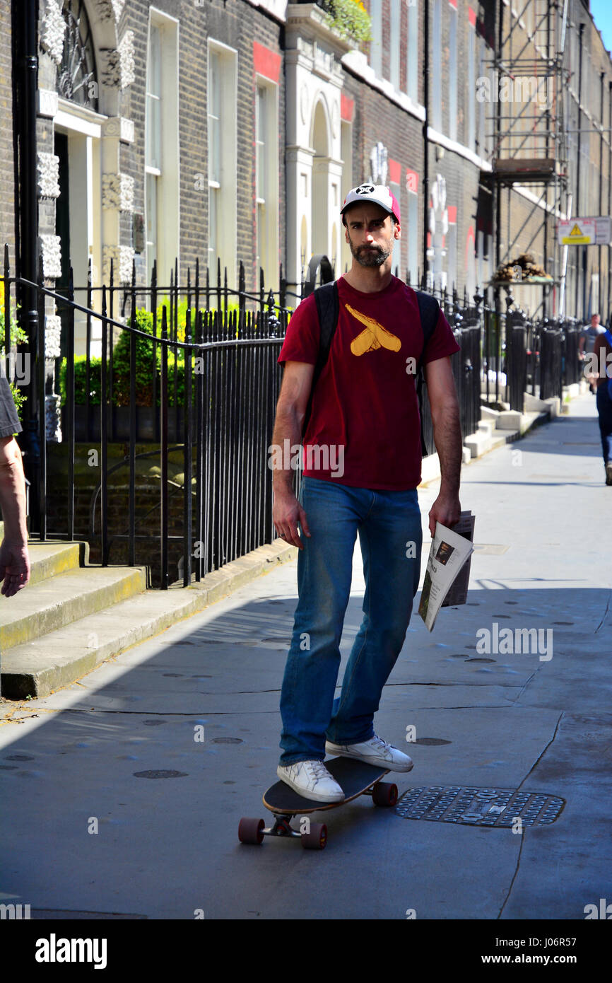 Homme avec un skateboard équitation journal sur le pavé à Londres, Royaume-Uni Banque D'Images