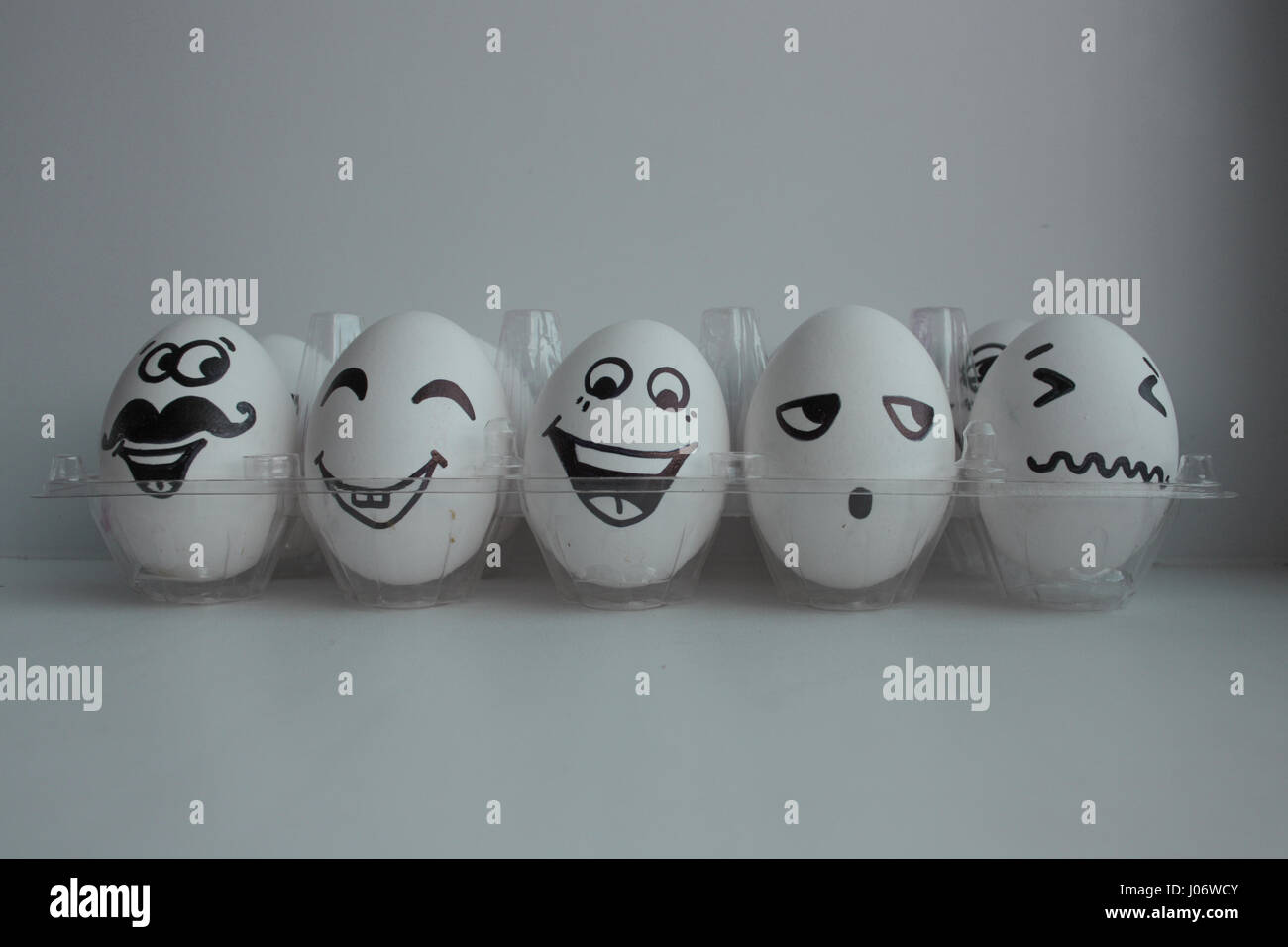 Oeufs de Pâques en blanc dans un groupe fort transparent avec bonne humeur et espiègle fait face à l'amusement. Cinq morceaux dans une rangée Banque D'Images