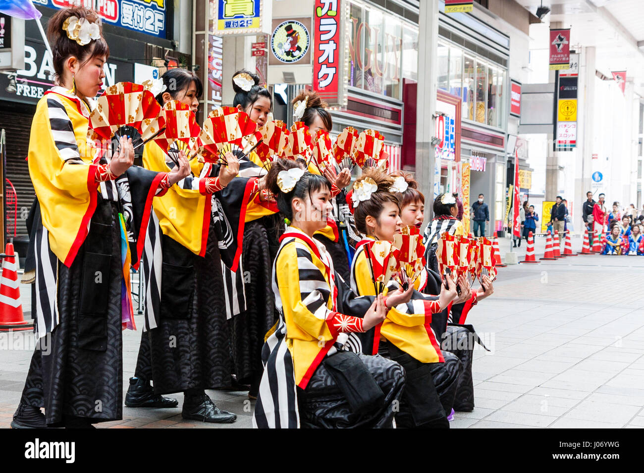 Le Japon, Kumamoto, Hinokuni danse Yosakoi Festival. L'équipe de femmes adolescentes, vêtu de noir et jaune, s'agenouiller et yukata holding fans, dans centre commercial. Banque D'Images