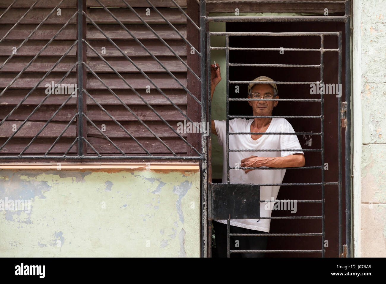 Un homme cubain à l'extérieur de sa maison par l'intermédiaire de barres de sécurité dans la Vieille Havane, Cuba. Banque D'Images