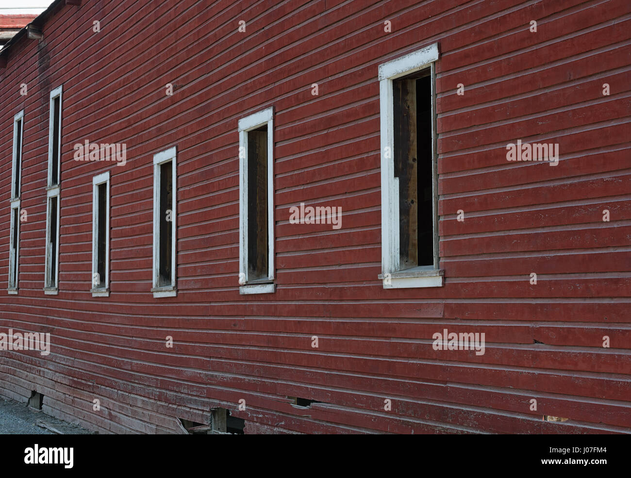 Une rangée de baies de fenêtre vide s'étendent en bas du côté d'un mur en bois peint rouge vieilli. Banque D'Images