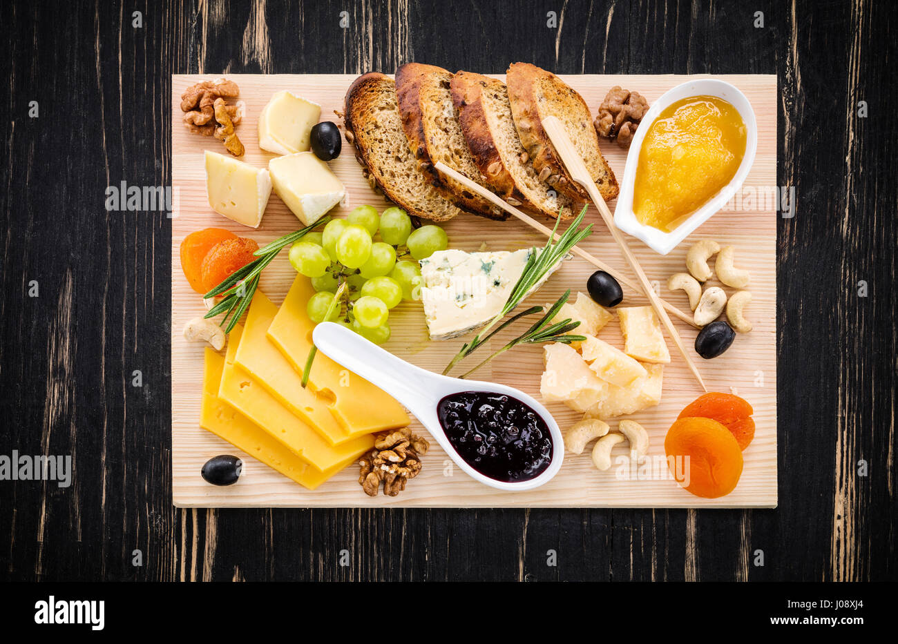 Assiette de fromage servi avec des tranches de pain, les raisins, les abricots secs, olives, confitures, miel et noix sur fond de bois Banque D'Images