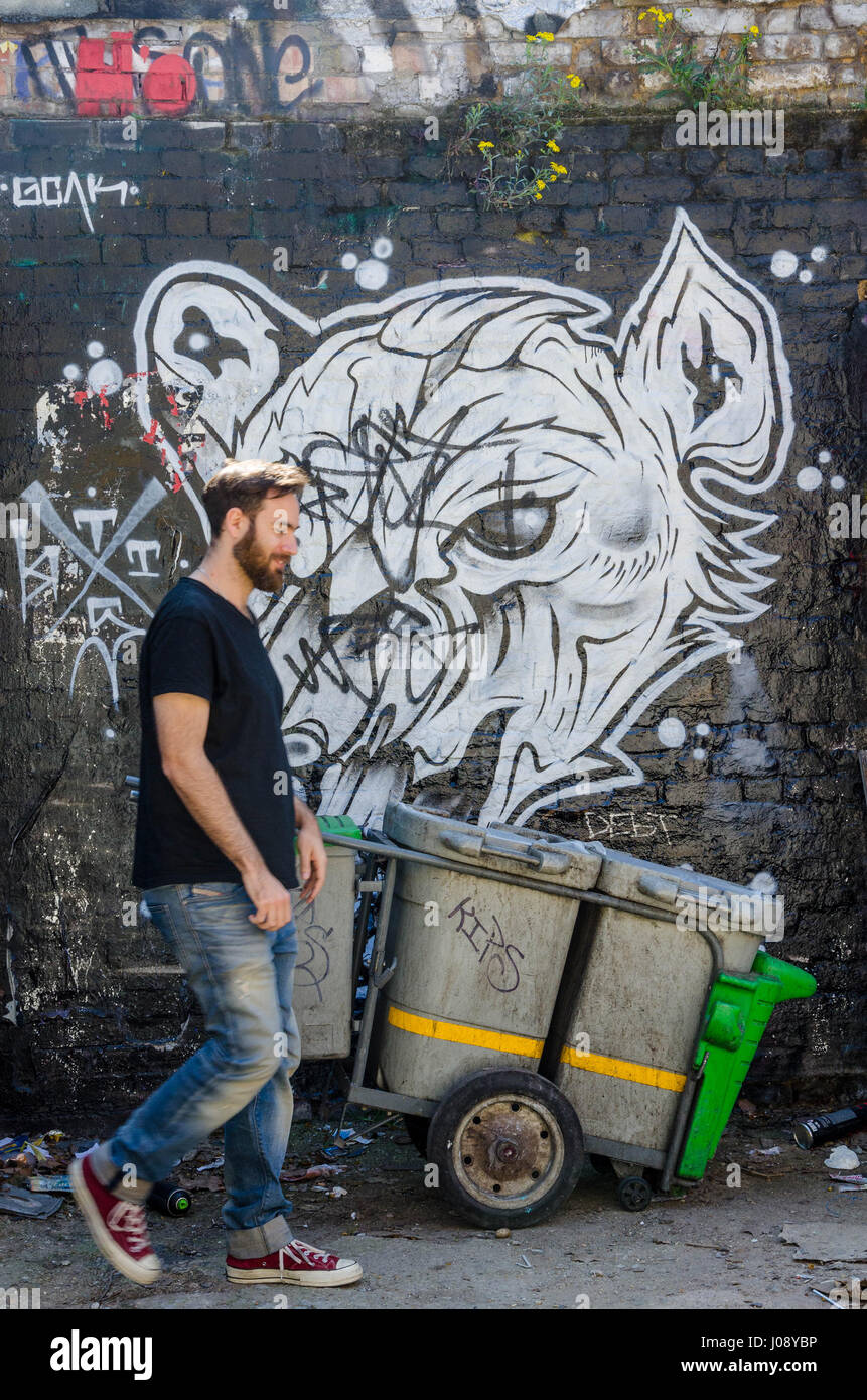 Un homme passe devant un camion de nettoyage de rue et en noir et blanc peinture murale peinte sur le mur d'une aire de stationnement au large de Brick Lane dans l'Est de Londres. Banque D'Images