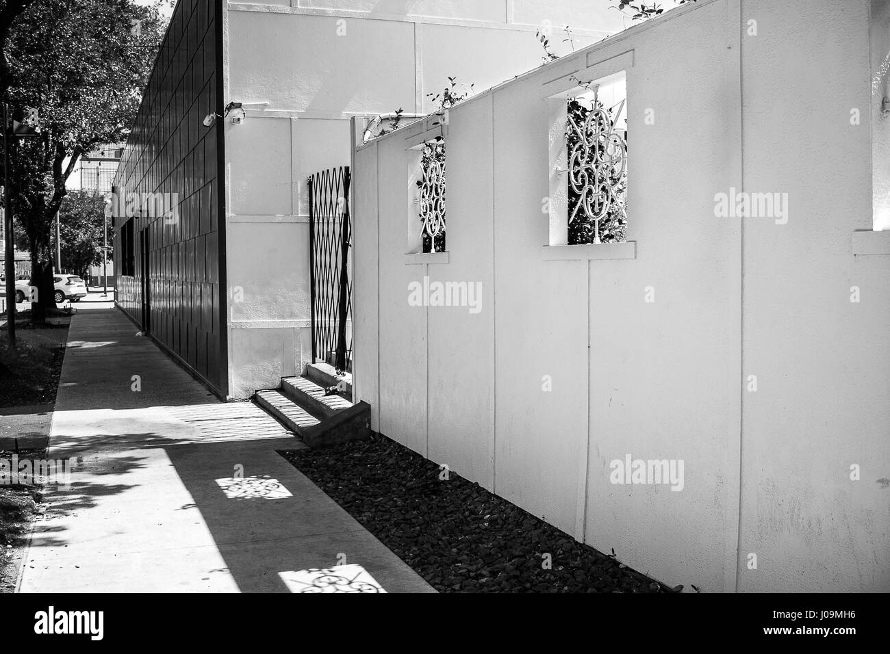 Le noir et blanc d'un long trottoir avec des ombres sur les fenêtres du mur voisin. Banque D'Images