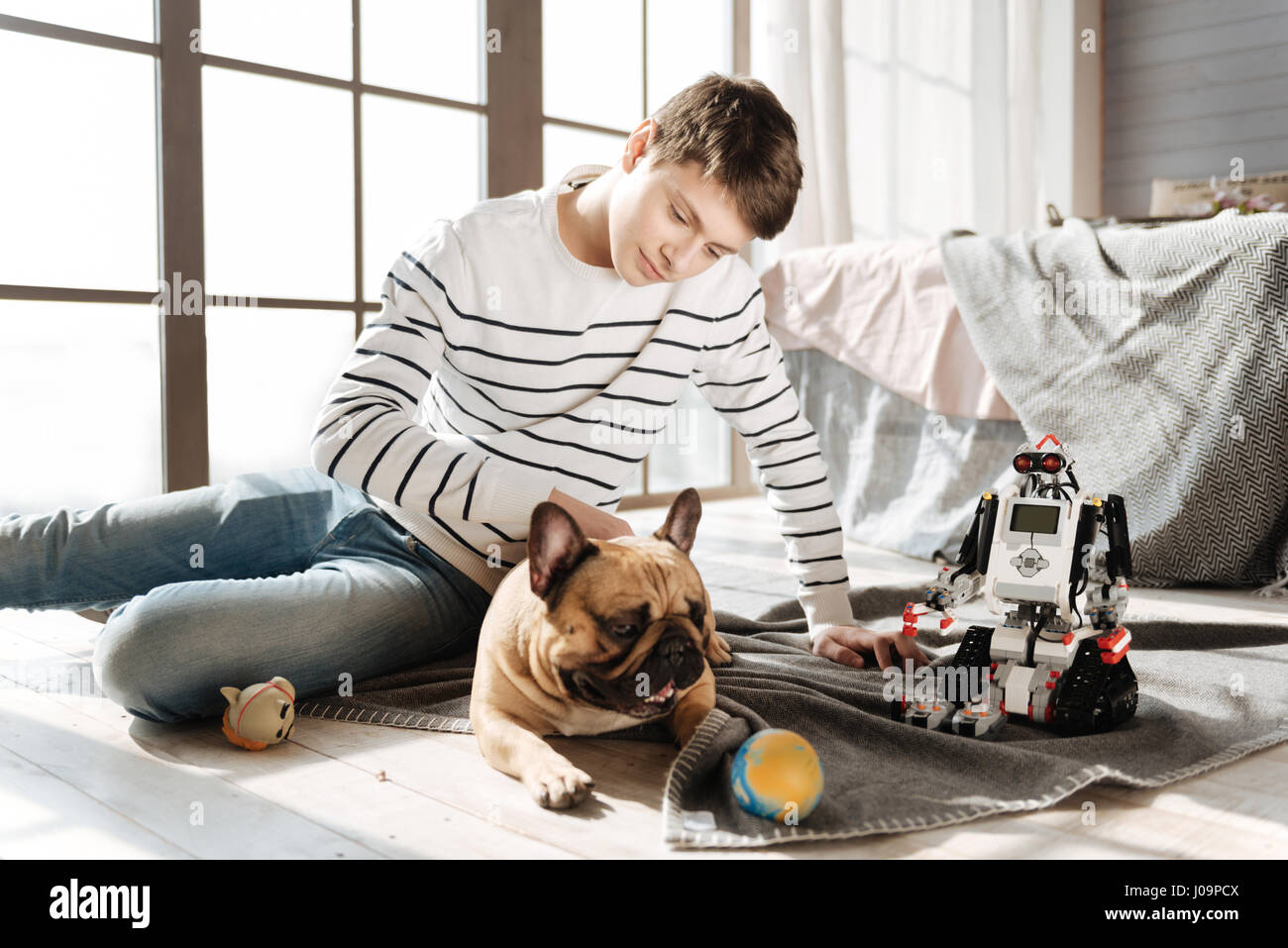 Bonne humeur. Joli garçon mettre main gauche près de son domicile en tapotant robot animal de compagnie tout en inclinant sa tête Banque D'Images
