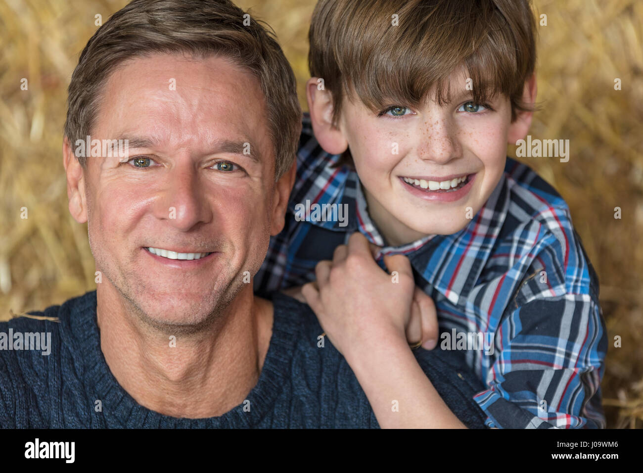 Portrait d'une belle réussite, et happy middle aged man homme vêtu d'un pull bleu assis sur des bottes de foin avec son enfant mâle boy fils dans un Banque D'Images