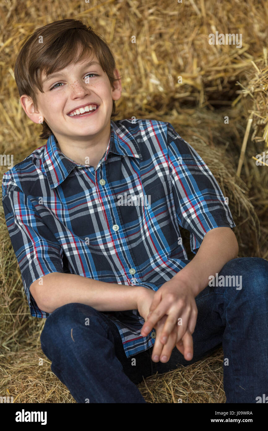 Young happy smiling boy avec dents parfait portant une chemise à carreaux et assis sur des balles de foin ou de paille Banque D'Images