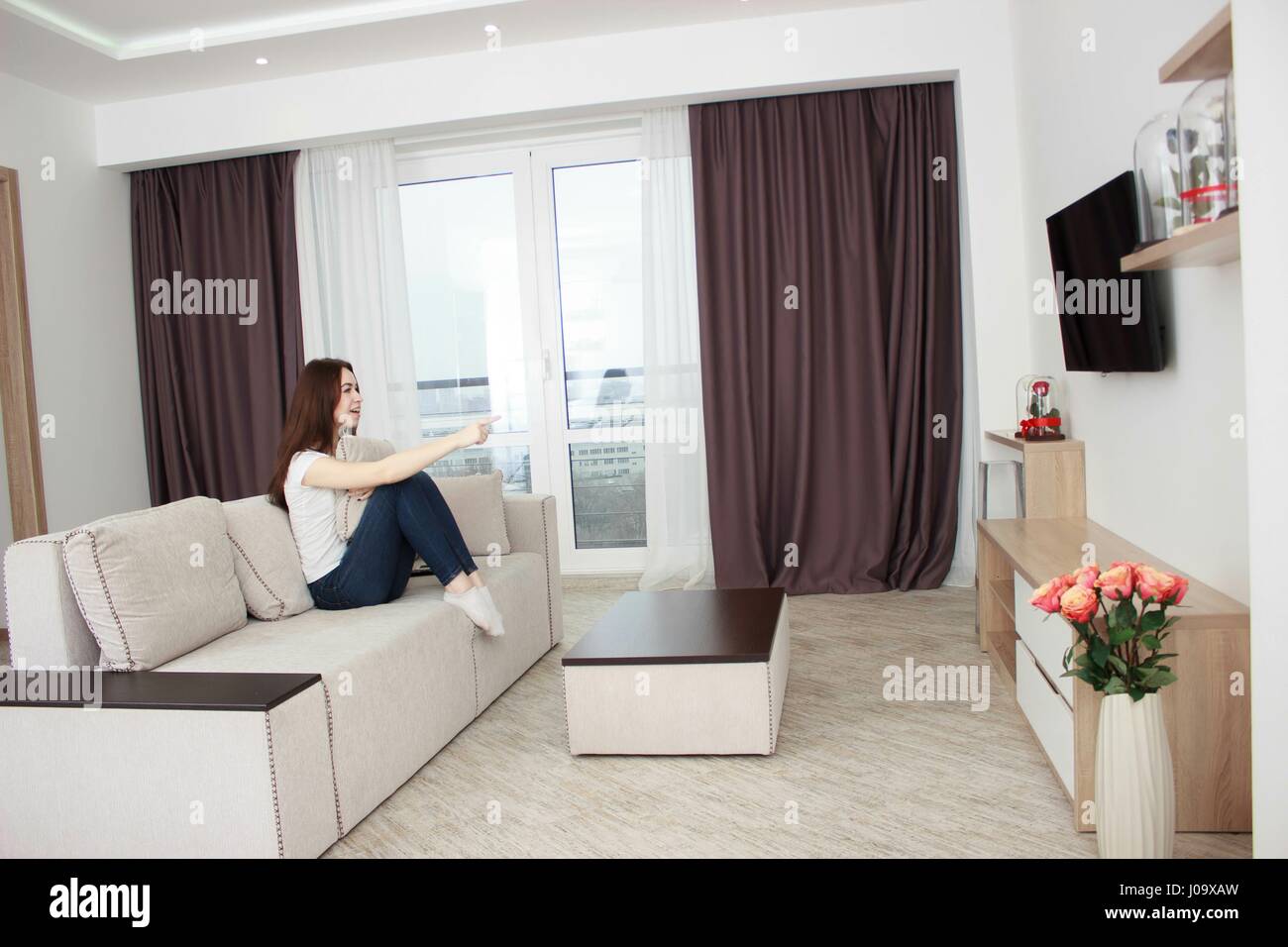 Peur jeune femme regardant la télévision. Brunette girl sitting on couch Banque D'Images