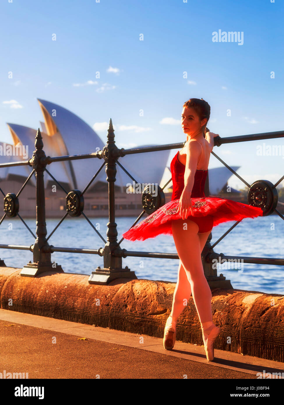 Street dance performing ballerine en rouge les concerts danse tutu au point de chaussures à une clôture du port de Sydney en rayons chauds du soleil du matin. Banque D'Images