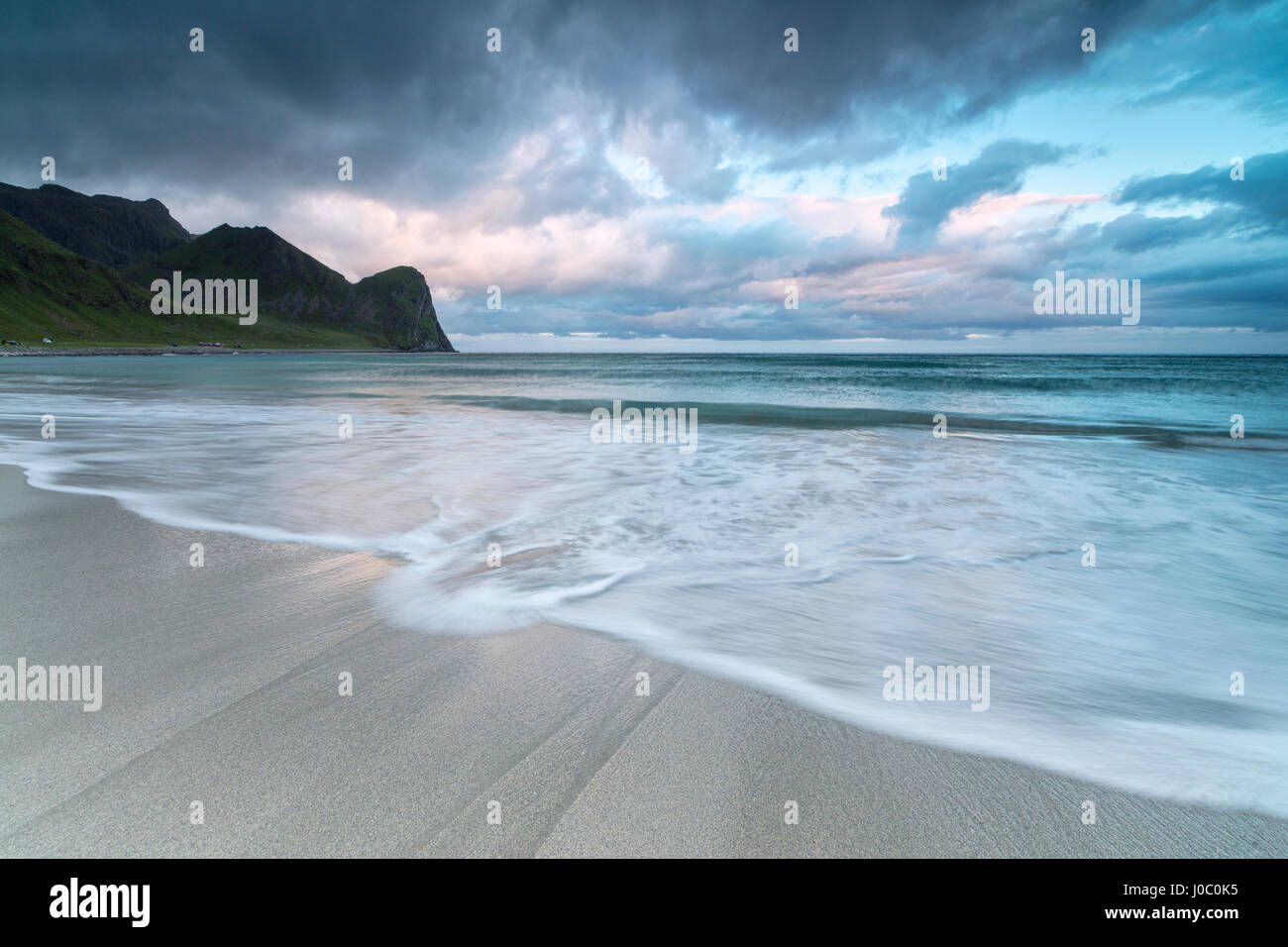Nuages rose de minuit Soleil reflété sur le bleu de la mer et de la plage de sable fin, Unstad, Vestvagoy, îles Lofoten, Norvège, de l'Arctique Banque D'Images