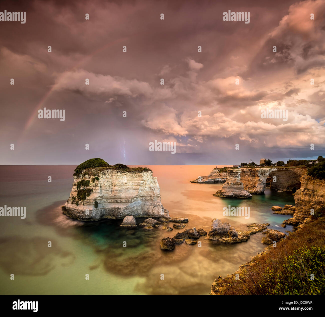 La foudre et arc-en-ciel après la tempête sur les falaises appelé Faraglioni di Sant'Andrea, province de Lecce, Pouilles, Italie Banque D'Images