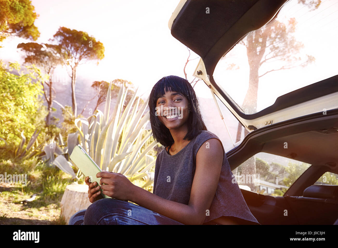 Portrait de jeune femme assise dans la voiture ouverte boot, holding digital tablet Banque D'Images
