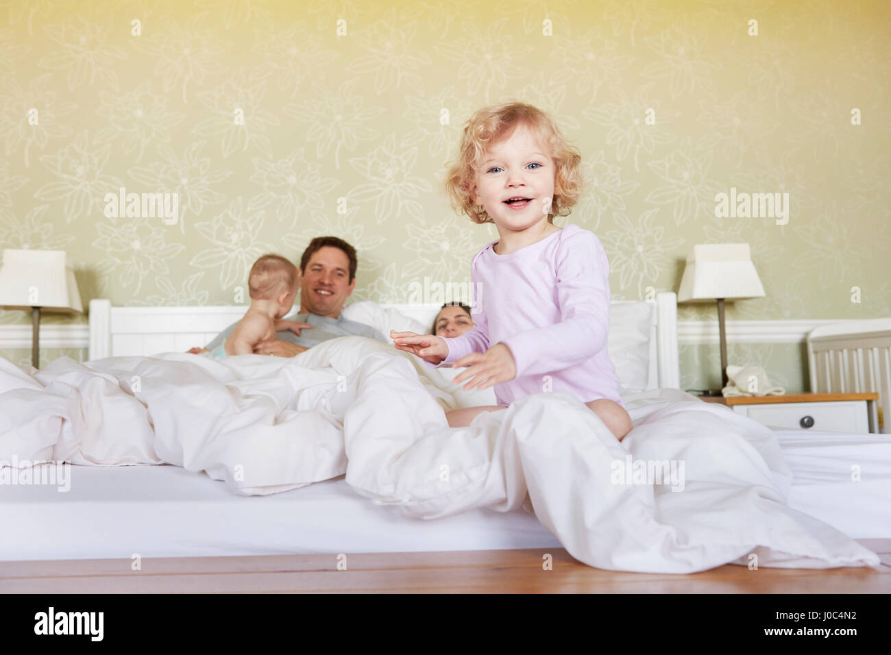Portrait of cute female toddler assis sur le lit avec les parents et petite soeur Banque D'Images