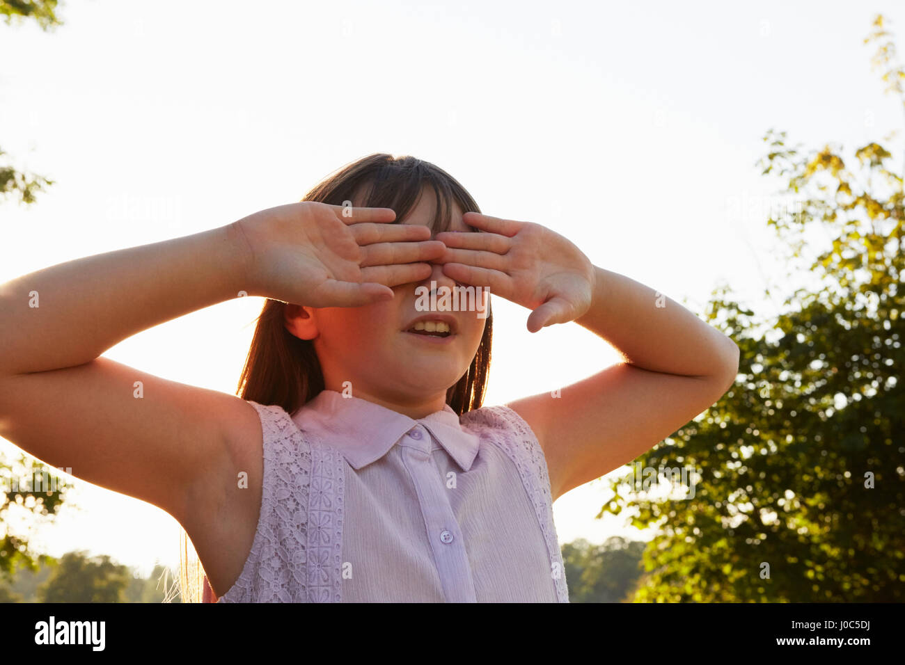 Girl couvrant les yeux pour masquer et chercher dans park Banque D'Images