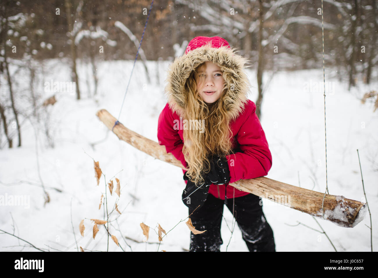 Girl leaning on wooden swing in woods Banque D'Images