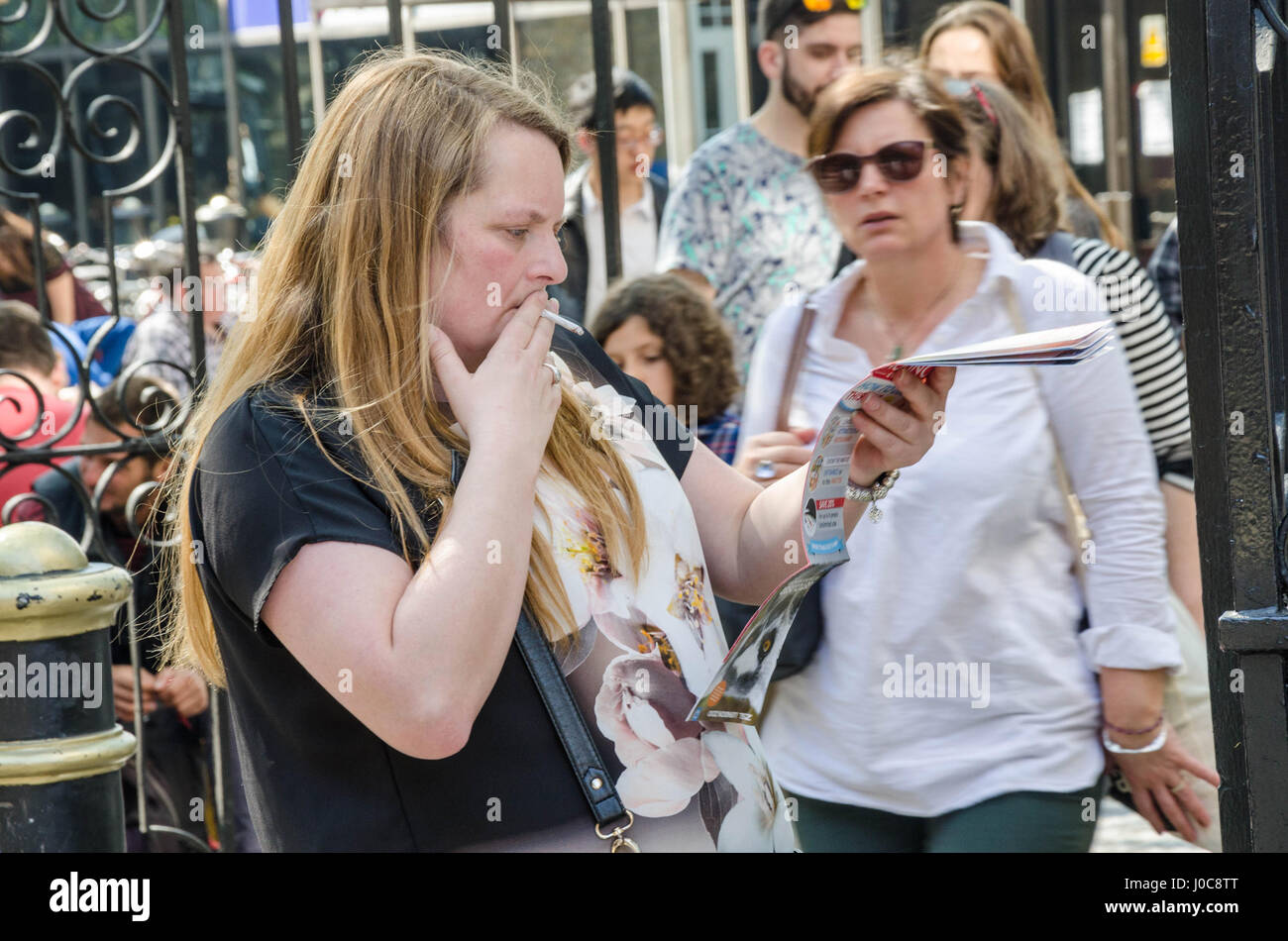 Une dame consulte un guide touristique brochure tout en fumant une cigarette dans la rue.. Banque D'Images