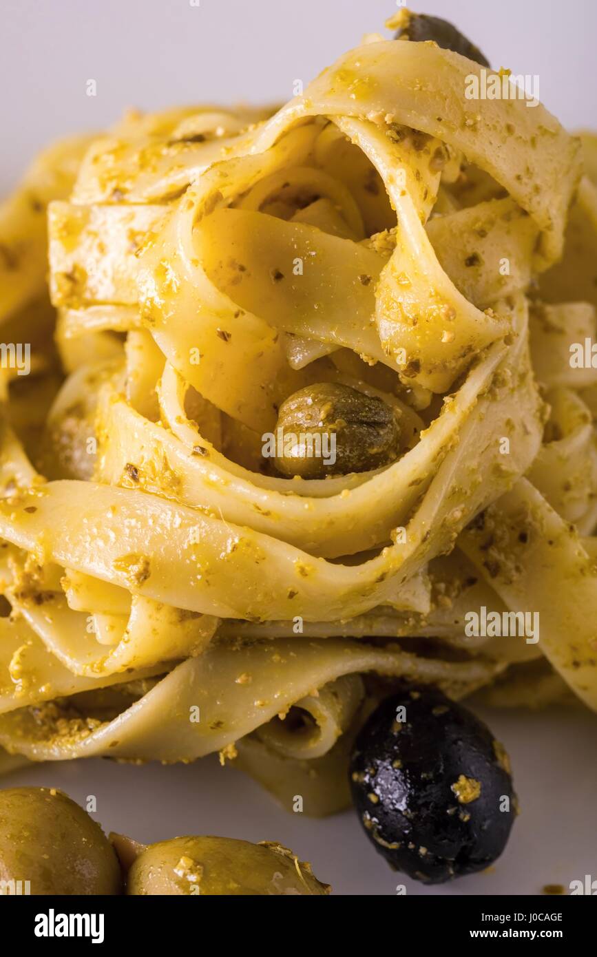 Photo verticale seule portion de tagliatelle avec pesto vert sur la plaque en céramique blanche. Les olives vertes et noires avec des amandes est renversé autour de Banque D'Images