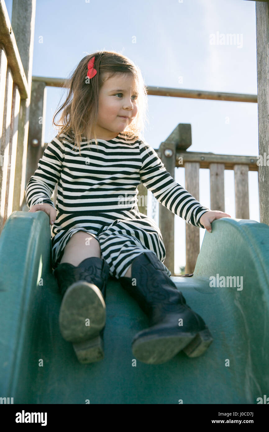 Jolie fille en robe rayée assis sur l'aire de glisse Banque D'Images