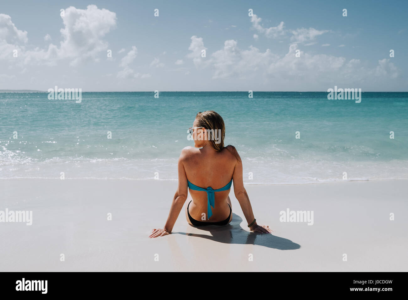 Rear view of woman in bikini sitting on beach looking out du blue sea, Anguilla, Saint Martin, Caraïbes Banque D'Images