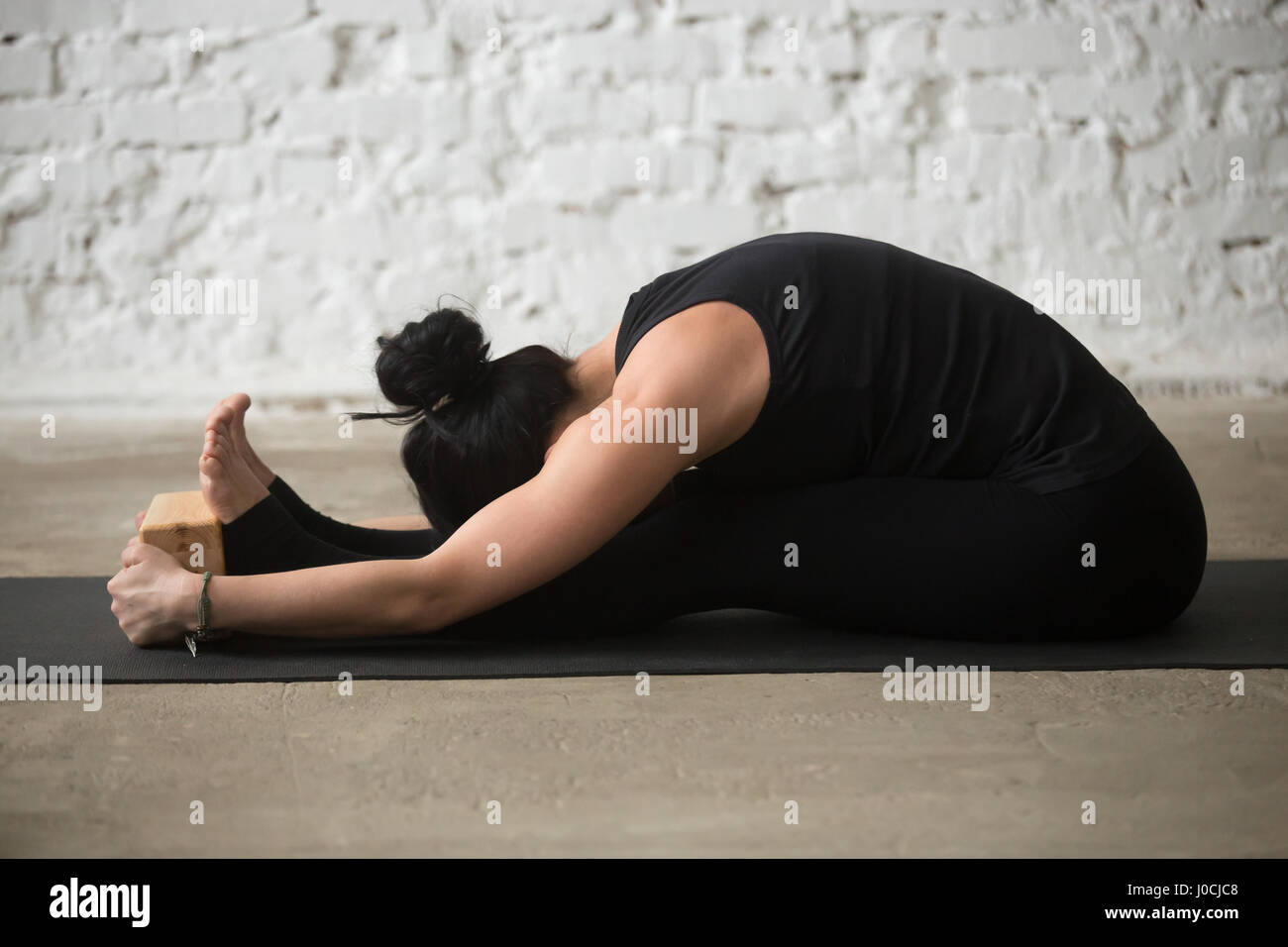 Jeune femme yogi dans paschimottanasana posent avec block, loft retour Banque D'Images