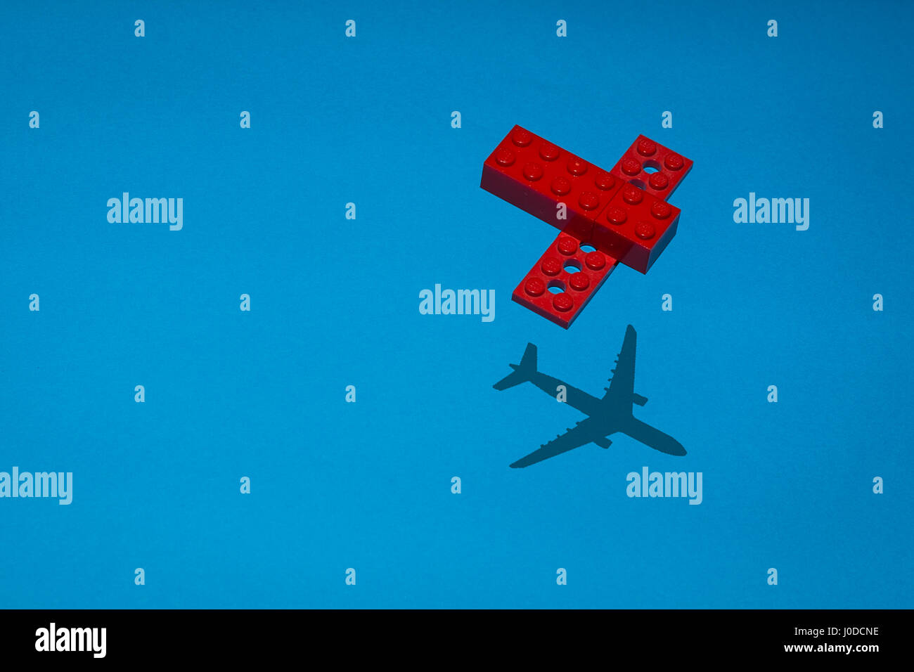 Avion construit en brique rouge de lego bleu sur une police avec l'ombre d'un vrai avion. Banque D'Images