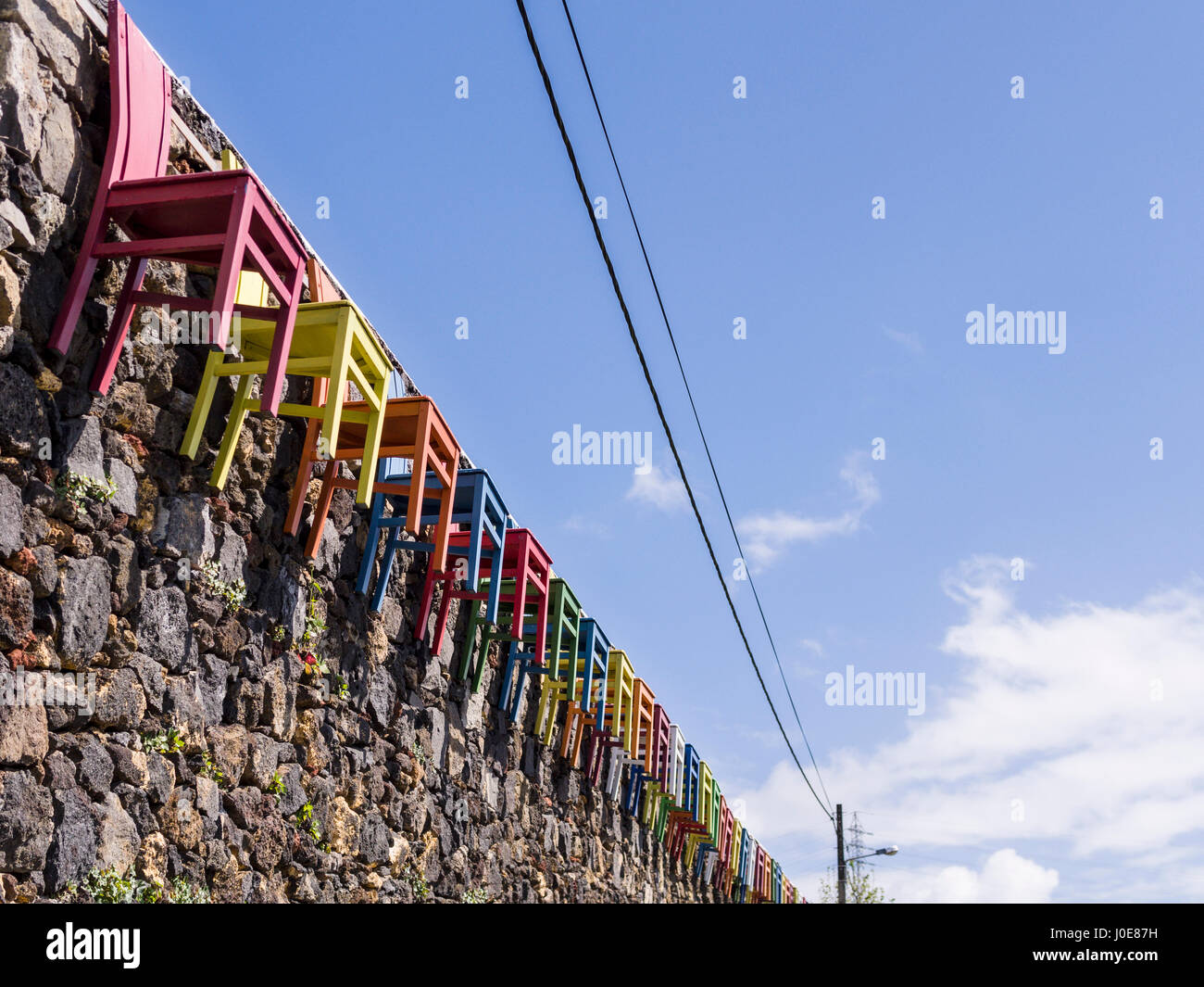 Chaises de couleur sur un mur de pierre. Une longue ligne de chaises en bois, peint en couleurs primaires vives arêtes un mur de pierre brute à Sao Roque près de la capitale. Banque D'Images