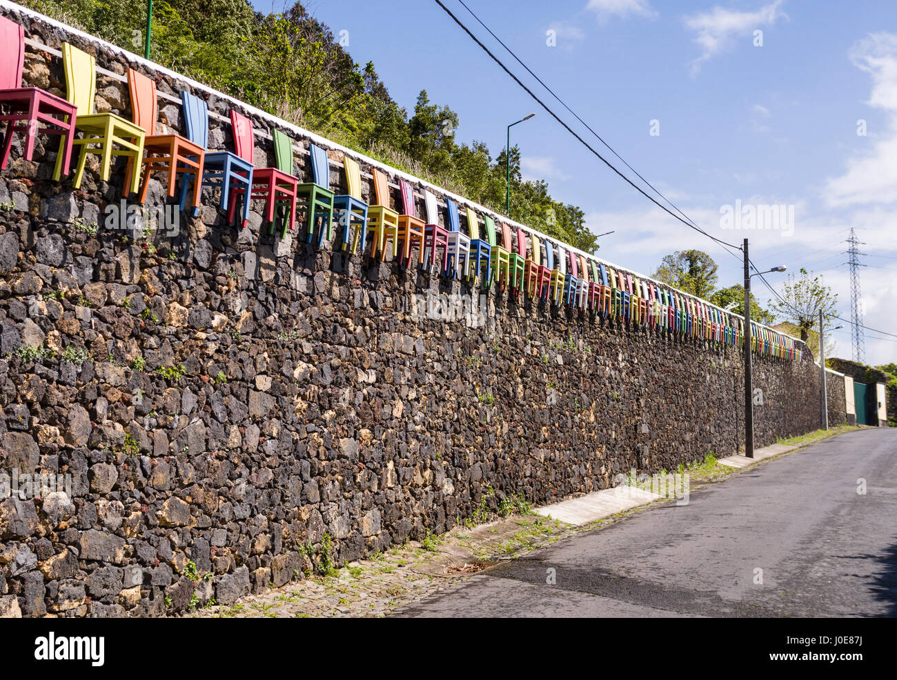 Chaises de couleur sur un mur de pierre. Une longue ligne de chaises en bois, peint en couleurs primaires vives arêtes un mur de pierre brute à Sao Roque près de la capitale. Banque D'Images
